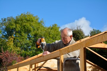 Man at work drilling woodwork outside on sunny day