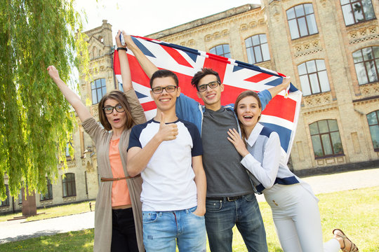 Group Of Students Holding A Flag Of Great Britain On The University Campus Background.