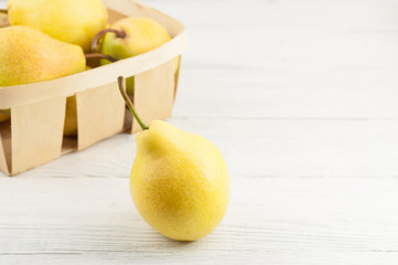Heap of fresh ripe yellow whole pears in wicker basket and one pear separately on old rustic white wooden table