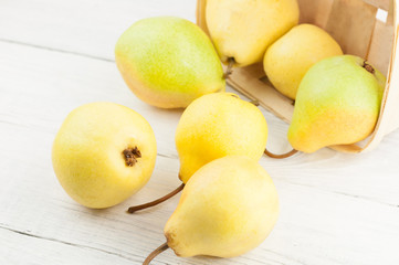 Lot of fresh ripe yellow whole pears poured out of wicker basket on old rustic white wooden table