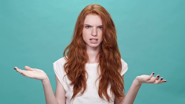Happy ginger woman in t-shirt covering her face and disappointed after that while looking at the camera over turquoise background