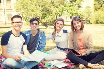 Group of young people discuss and talk. Students sitting on a clearing in the campus.