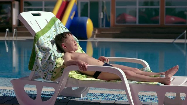 Boy resting and taiking sunbathe on a lounger in the aquapark near the pool