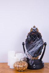 Copy space. A decorative mirror covered with cobweb. A decorative golden pumpkin and LED white pillar candles. 