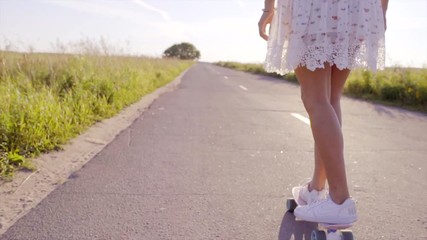 Young beautiful woman is skating on the skateboard at sunset on the country road - Powered by Adobe