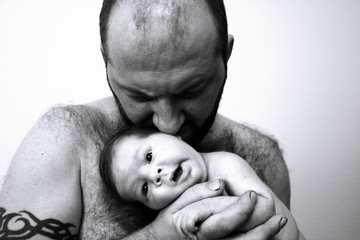 Portrait of strong Father kissing naked newborn dumbfounded baby close up black and white. 