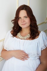 Beautiful pregnant woman  dressed in white dress and jewelry with hand on belly