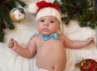 Baby first christmas. Beautiful little baby in Santa hat and bow tie lays on white background framed with christmas tree needles and balls. New Year's holidays. Santa baby.