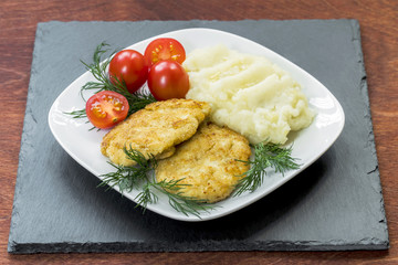 Two juicy fried meat patties on a white plate with cherry tomatoes and mashed potatoes.