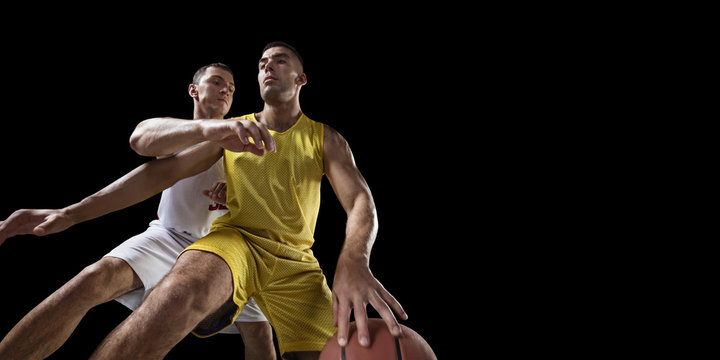 Two basketball players fight for the basketball ball. Isolated basketball players on a black background. Player wears unbranded clothes. Bottom view. © Alex