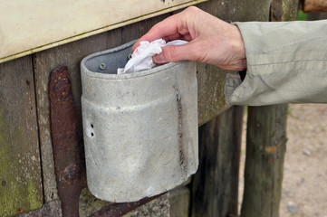 An elderly rural woman throws a crumpled dirty napkin into a small metal trash can