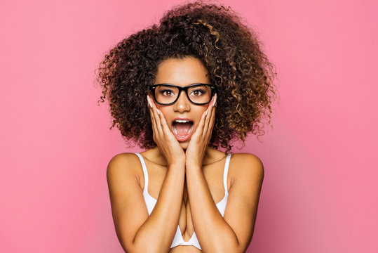 Surprised beautiful black woman holds cheeks by hand and wear glasses
