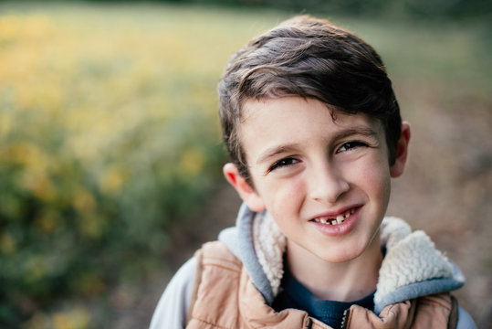 A young boy exploring and playing outside in the country and fields, smiling with a missing front tooth