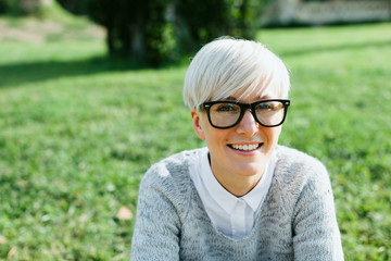 Blonde woman wearing rimmed glasses sitting on the park.