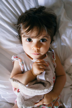 Serious baby girl lying on a bed holding her dou dou, from above
