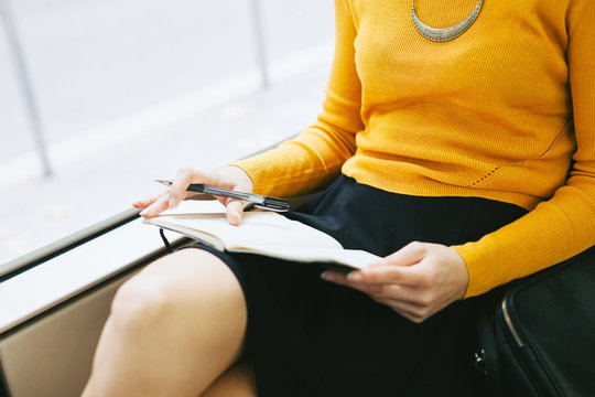 Closeup of a chic woman writing on her notebook sitting in the train.