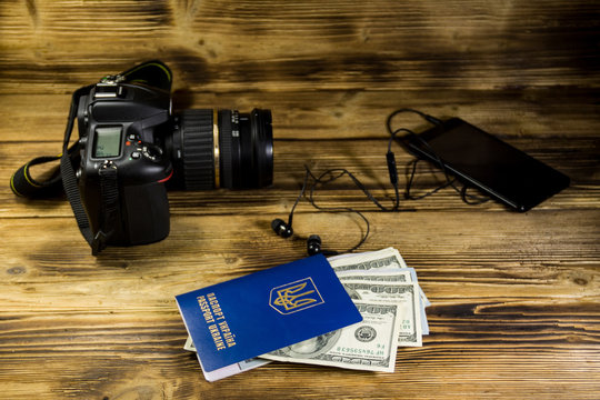 Traveling concept with smart phone, headphones, ukrainian passport, dollars and camera on wooden desk