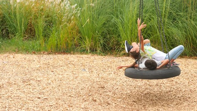 happy brother and sister swinging on a swing on the amusement park in the city. 4k, copy space, slow motion. life style