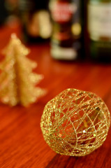 Golden Christmas ball for decoration on wooden table with bottle of drink in the background