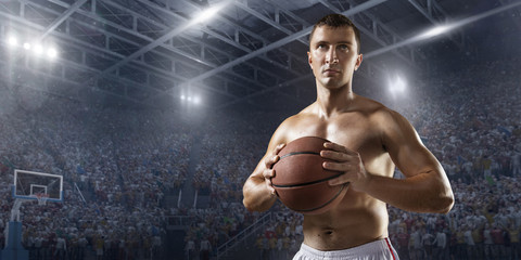 Fototapeta na wymiar Basketball player hold a basketball ball on big professional arena. Basketball player with a naked torso and pumped muscles. Player wears unbranded clothes.