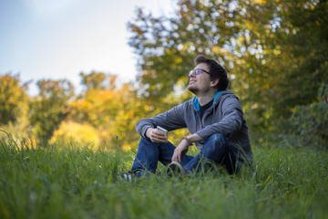 Naklejka na ściany i meble Junger Mann sitzt im Gras, Smartphone, entspannt und nachdenklich, Textfreiraum
