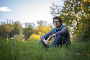 Junger Mann sitzt im Gras, entspannt und nachdenklich, Textfreiraum