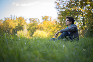 Naklejka na ściany i meble Junger Mann sitzt im Gras, entspannt und nachdenklich, Textfreiraum