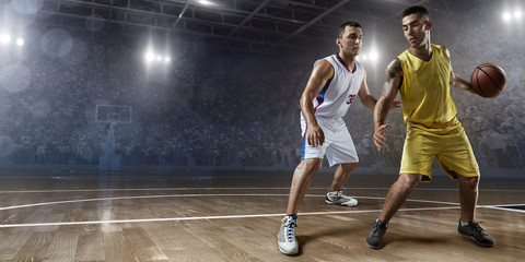 Two basketball players fight for the basketball ball on big professional arena. Player wears unbranded clothes.