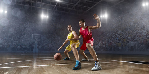 Two basketball players fight for the basketball ball on big professional arena. Player wears unbranded clothes. © Alex