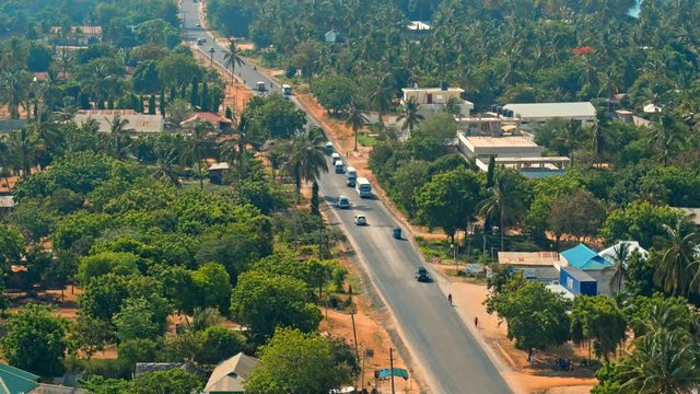 Cinematic aerial of busy traffic on streets of city of Dar es Salaam by Indian ocean in Tanzania, Africa. Cars, busses, motorcycles, pedestrians, lush, green vegetation, palm trees, hot summer day