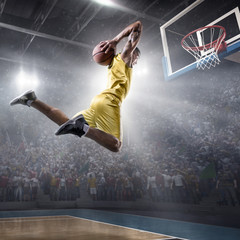 Basketball player makes slam dunk on big professional arena. Player flies through the air with the ball. Player wears unbranded clothes. © Alex