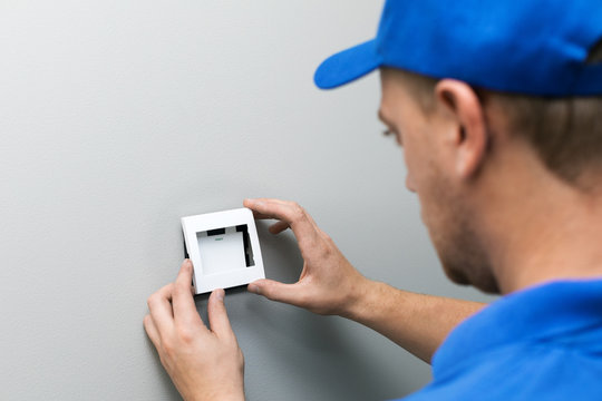 electrician in blue uniform installing light switch on the wall