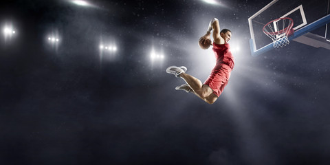 Basketball player makes slam dunk on big professional arena. Player flies through the air with the ball. Player wears unbranded clothes. © Alex