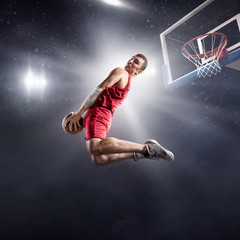 Basketball player makes slam dunk on big professional arena. Player flies through the air with the ball. Player wears unbranded clothes. © Alex