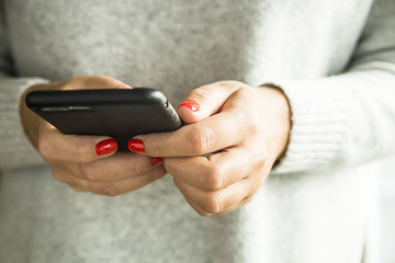 girl with red nails holding a smartphone in a black case
