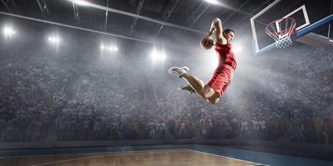 Basketball player makes slam dunk on big professional arena. Player flies through the air with the ball. Player wears unbranded clothes.
