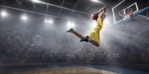 Basketball player makes slam dunk on big professional arena. Player flies through the air with the ball. Player wears unbranded clothes. © Alex