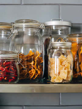 A close shot of dried or dehydrated peppers and fruits in glass jars sitting on shelf in a kitchen.