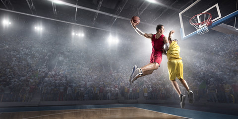 Fototapeta na wymiar Basketball player makes slam dunk on big professional arena. Player flies through the air with the ball. Opponents try to prevent the ball from hitting the basketball ring.