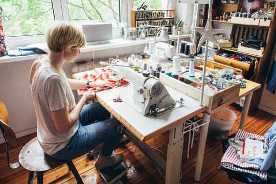 Blond Caucasian Woman Working on Sewing Machine in Bright Dressmaking Atelier
