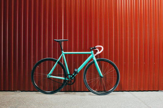 Minimalist Turquoise Fixed Gear Bicycle Leaning Against Shiny Red Metallic Wall