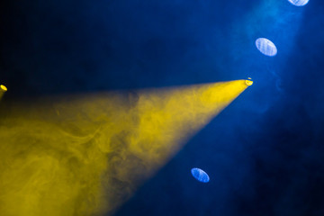 Yellow and blue light rays from the spotlight through theatrical smoke. Lighting equipment on the stage.