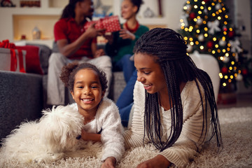 smiling sisters are playing with dog They are lying on floor near Christmas tree.