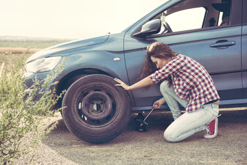 .Beautiful young woman changing tires on her car