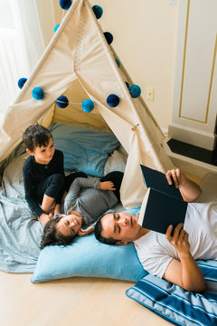 father reading to his children in a comfortable teepee fort