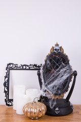 Halloween decorations. A decorative mirror with cobweb, a trio of pillar candles and a faux frame. A golden glass pumpkin. Copy space