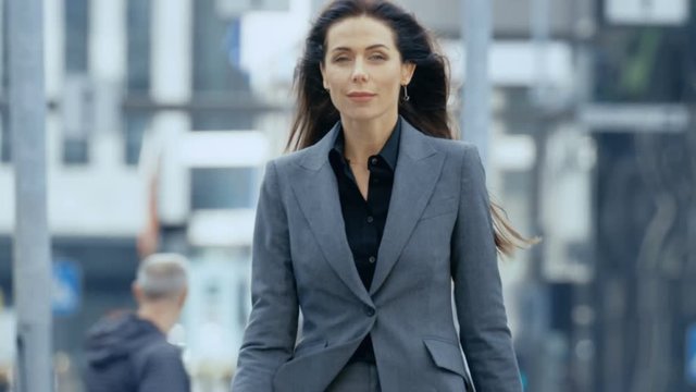 Medium Shot of the Business Woman in the Tailored Suit Walking on the Busy Big City Street in the Business District, Checks Her Smartphone. Confident Woman on Her Way to do Big Business. 4K UHD.