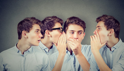 Three young men whispering each other and to shocked astonished guy in the ear.