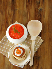Red caviar in a white ceramic bowl and a wooden spoon on a wooden table