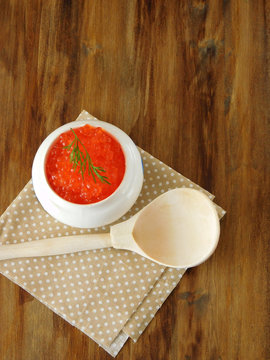 Red caviar in a white ceramic bowl and a wooden spoon on a wooden table